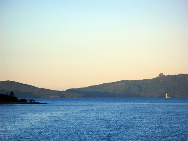 a boat with a bright yellow sail sailing on a sunny evening