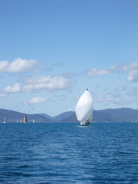 a yacht sailing with a large white spinnaker sail over a calm ocean