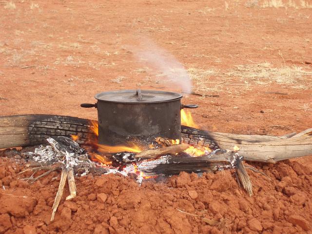 a heavy metal pot boiling on a camp fire