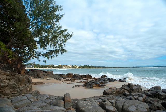 Noosa beach waterfront with a rocky shoreline and breaking waves on a cloudy day