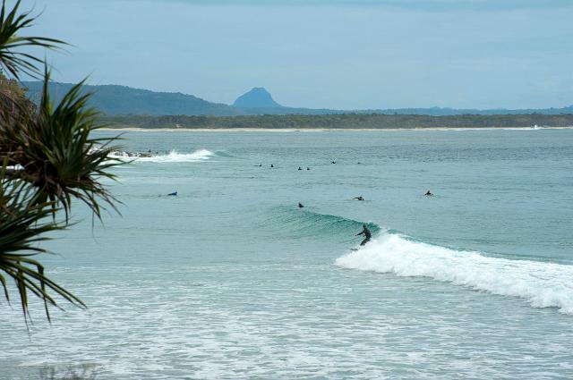 View of breaking waves with aurfers at Noosa beach in Queensland, Australia with Mt Cooroora in the background