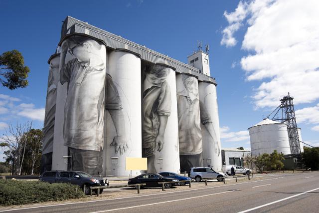 The Coonalpyn grain silos on the Dukes Highway, South Australia decorated with murals of men in a street view with parked cars