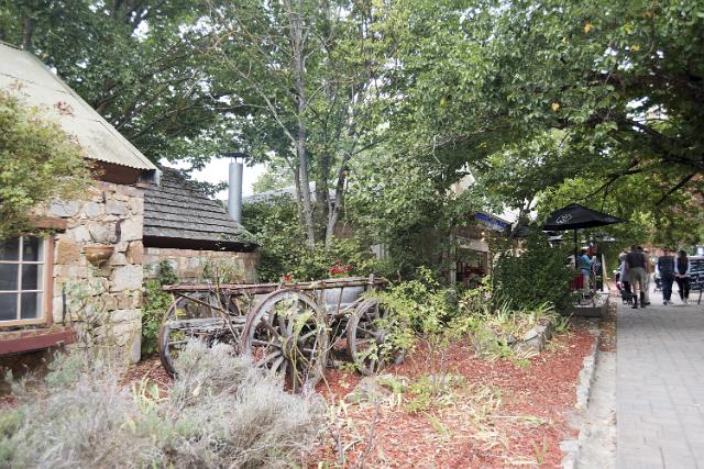 Old vintage wooden cart or wagon with decorative flowers in a garden at the edge of a street in Hahndorf, Australia alongside a historical stone building