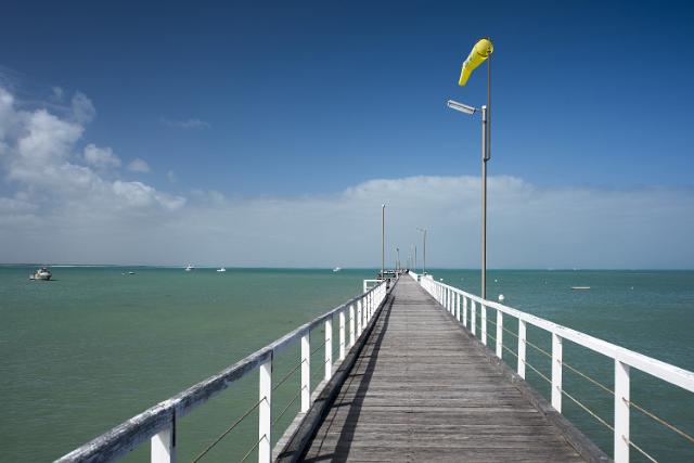 Receding view along the boardwalk on the pier, Beachport, South Australia with a wind sock fluttering in the breeze ans boats on the ocean in the distance