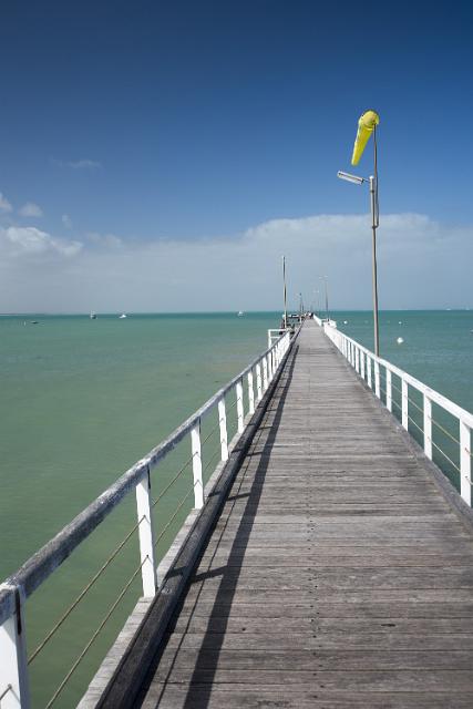 The long beachfront jetty or boardwalk at Beachport, Australia extending away into the ocean with a yellow wind sock against a blue sky