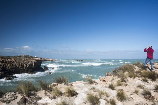 Man taking a photo of the cliffs at Robe, South Australia standing on a headland lookout or viewpoint overlooking the coastline