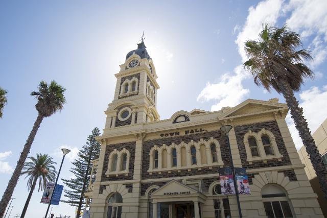 The front facade of the Town Hall, Glenelg, Adelaide, South Australia with its arched windows and clock tower flanked by tall tropical palm trees